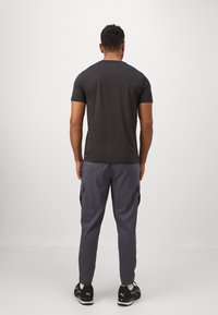 Kortsleeve mørkegrå t-skjorte sammen med grå cargo-bukser med sidelommer, akkompagnert av svarte joggesko.