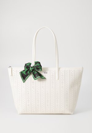 Witte tote bag met een gladde textuur, voorzien van geperste verticale tekst en een groene luipaardprint strikaccent. Dubbele handvatten voor het dragen.