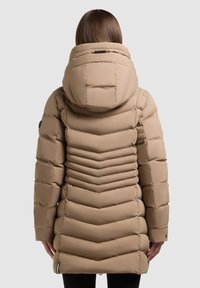Beige pufferjakke med hætte, der har et chevron-quiltet design og lange ærmer. Stoffet er glat med en let skinnende finish.