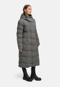 Vadderad lång kappa i grått med huva, med ett quiltat mönster och framfickor. Matchas med knähöga svarta stövlar.