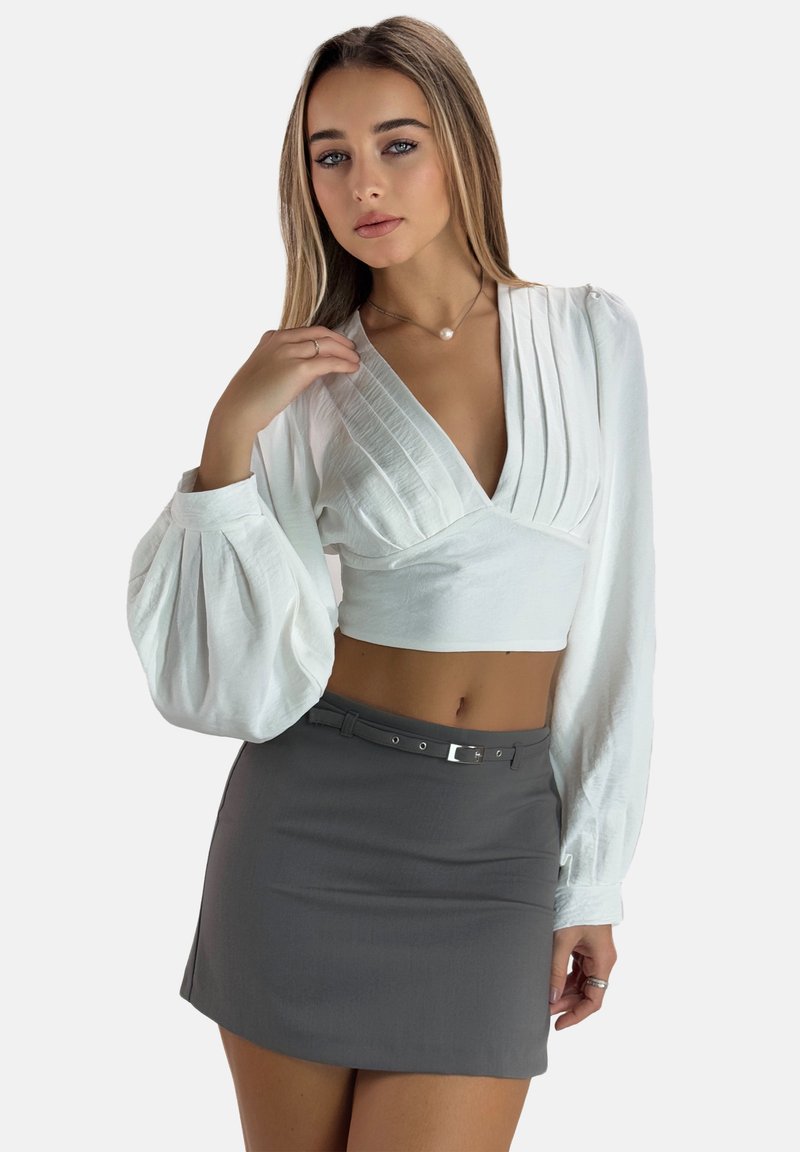 Witte gecropte wikkelblouse met plooien, gecombineerd met een grijze minirok met een riem en zilveren gesp. Glad materiaal met een getailleerd ontwerp.