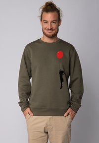 Olivengroene sweatshirt met een zwarte silhouet van een kind dat een rode ballon vasthoudt. Gemaakt van zacht materiaal met ribgebreide manchetten en zoom.