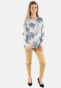 Bluză cu mânecă lungă, florală, de culoare albastru deschis pe un fundal alb; asociată cu pantaloni bej și tocuri negre; cu nasturi în față și guler.
