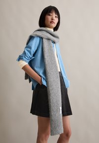 Grijze wollen sjaal gedrapeerd over een lichtblauw gestreept overhemd met knopen, gedragen met een zwarte corduroy rok; zachte textuur en ontspannen pasvorm.