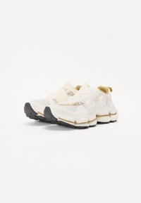 Kremowe buty sportowe z teksturowaną cholewką, amortyzowaną podeszwą i czarną gumową podeszwą. Charakteryzują się wyjątkowymi zaokrąglonymi detalami i akcentami.