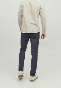 Vaateet: vaalean värin pitkähihaine paita ja tummansiniset housut. Housut ovat kapeat. Jalkineet ovat vaaleat ja niissä on karkea pohja.