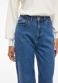 Μπλε τζιν παντελόνα ψηλής μέσης με χαλαρή εφαρμογή, διαθέτει κλείσιμο με κουμπί στο μπροστινό μέρος, θηλιές ζώνης και δύο πλάγιες τσέπες. Υφασμάτινη υφή.