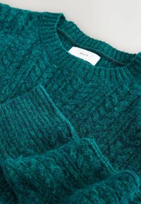 Struktuurne smaragdroheline sviiter, millel on ribakujuline ümardatud kaelus. Omab tihedat kudumismustrit ja sildi "NEXT". Pehme villane segu materjal.