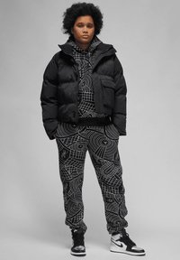 Zwarte gewatteerde jas over een zwarte geblokte hoodie en zwarte sweatpants met witte graphics. Zwarte en witte hoge sneakers maken de look af.