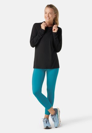 Black long-sleeve top, teal leggings, and light blue athletic shoes. The top features a round neck, leggings are fitted. Smooth texture.