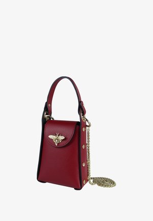 Sac à main en cuir rouge au design structuré, orné d'un accent abeille en or, avec des finitions noires et une bandoulière chaîne dorée amovible. Comprend une fermeture à pression et des clous décoratifs.