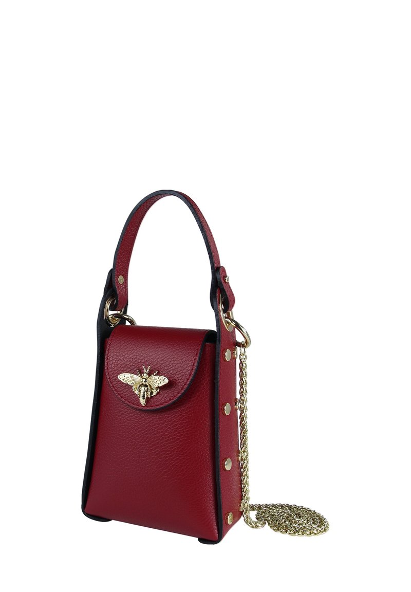 Sac à main en cuir rouge au design structuré, orné d'un accent abeille en or, avec des finitions noires et une bandoulière chaîne dorée amovible. Comprend une fermeture à pression et des clous décoratifs.