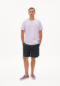 T-shirt en coton lilas clair, shorts navy et chaussures d slip-on violettes. La tenue présente une coupe décontractée avec des manches courtes et un col rond.