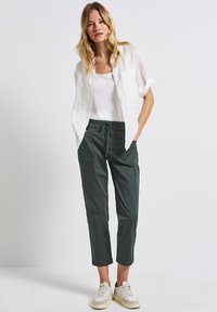 Lätt vit linneskjorta, gröna byxor med dragsko och två framfickor, samt avslappnade krämfärgade sneakers. Enkel, avslappnad passform.