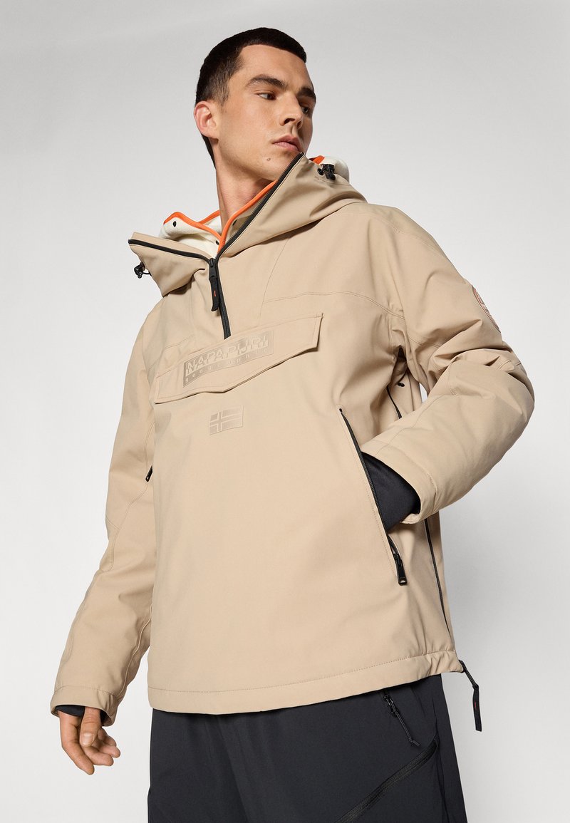 Veste imperméable beige avec un col haut, une capuche réglable, des poches zippées et un détail de logo à l'avant. Présente une doublure orange contrastante.