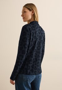 Marineblauwe blazer met luipaardprint, lange mouwen en een kraag, met een soepele textuur en een getailleerd ontwerp, gecombineerd met blauwe jeans.
