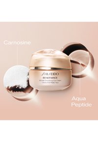 Shiseido Benefiance Wrinkle Smoothing Eye Cream i en rund, frostad glasburk med ett guldlock. Innehåller vita pulver och mörka vätskeeingredienser.