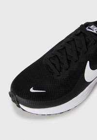 Sorte Nike joggesko med hvit såle og Nike swoosh-logoer på tå og side, litt vinklet på en enkel hvit bakgrunn.
