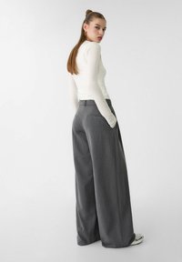 Graue, weit geschnittene Hose mit taillierter Passform, ausgestattet mit Seitentaschen und einem Bund. Kombiniert mit einem figurbetonten Langarmoberteil.