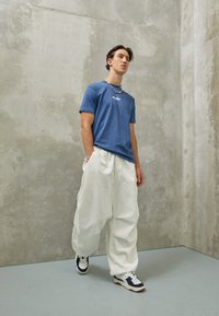 Blå bomulds-T-shirt med korte ærmer og hvidt logo, parret med oversized hvide bukser og marineblå sneakers med hvide accenter.