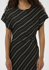 Mustmustärk must outfit, millel on valged diagonaalsed triibud, pehme kangas, lühikesed alustelgiga varrukad, sõlme detail vööl ja lõdva siluett.