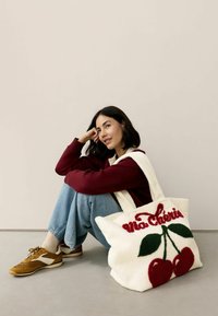 Hvid, fluffy tote bag med røde kirsebærdesigns og teksten "Ma Chérie". Tasken har to robuste håndtag og et rummeligt indre.
