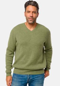Pull en v olive avec texture côtelée et manches longues, associé à un jean bleu. Conçu pour un ajustement décontracté.