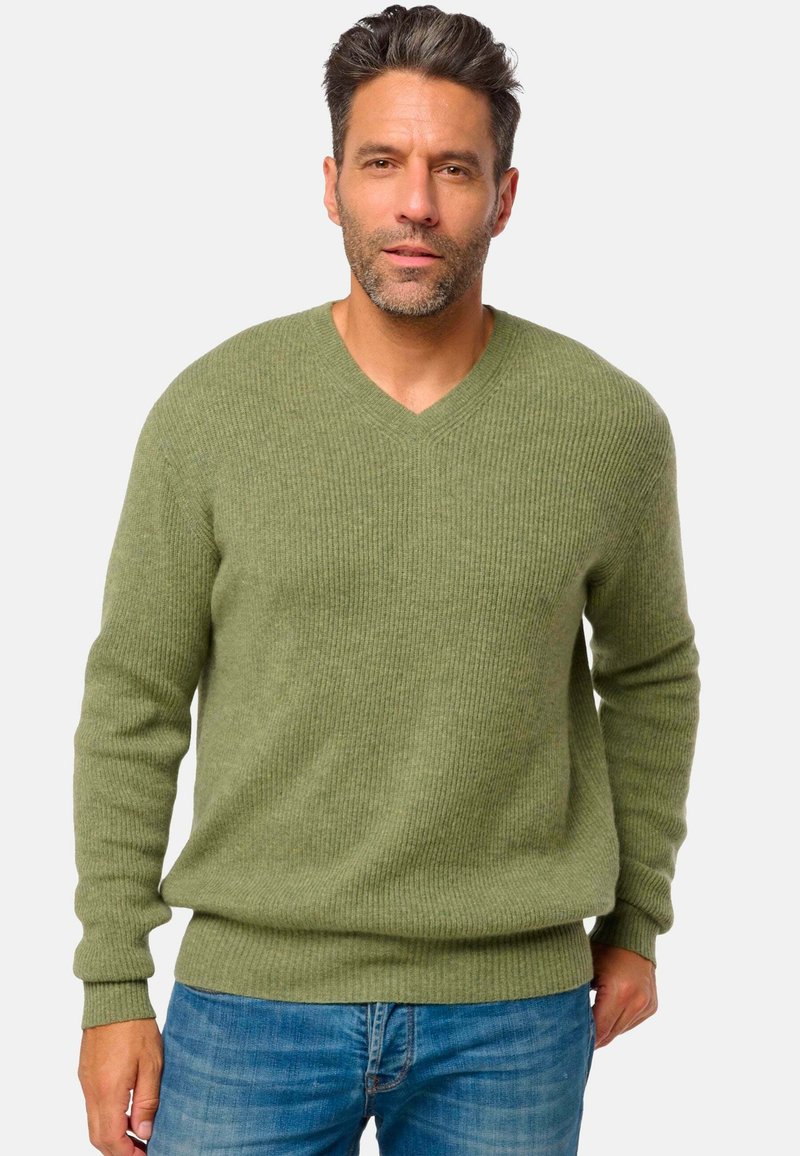 Pull en v olive avec texture côtelée et manches longues, associé à un jean bleu. Conçu pour un ajustement décontracté.