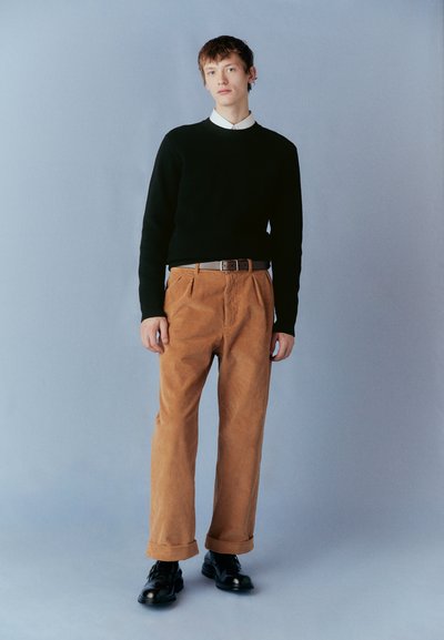 Pulover negru din tricot, pantaloni din catifea cu pliuri de culoare bej, curea maro și pantofi negri. Design simplu, formă ajustată și manșete de pantalon răsucite.