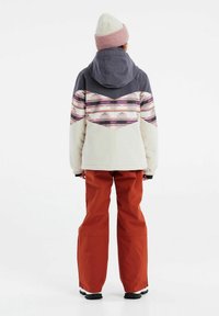 Veste à capuche avec un design imprimé au dos en crème, gris et rose, associée à un pantalon orange et des bottes de neige noires.