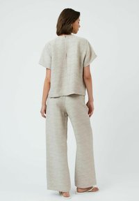 Ensemble deux pièces beige clair comprenant un top à manches courtes et un pantalon ample, fabriqué dans un tissu texturé avec un design décontracté et un détail de fermeture éclair au dos.