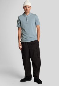 Lichtblauw polo shirt met drie knopen en geborduurd logo, gecombineerd met zwarte cargo broek met zijzakken en een relaxte pasvorm.