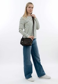 Svart läderaxelväska med beige detaljer, i kombination med en vit och grön randig långärmad skjorta och ljusblå jeans.