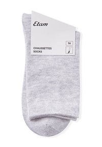 Calcetines gris claro hechos de un material suave y texturizado con un puño acanalado. Incluye una etiqueta de papel rectangular con detalles de la marca y del producto.