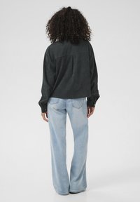 Schwarzes Denim-Hemd mit einer lockeren Passform, ausgestattet mit einem Rückenfalte und geknöpften Manschetten; kombiniert mit hellblauen, weit geschnittenen Jeans mit subtilen Verwaschungen.