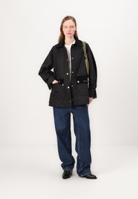 Quilted black jacket with gold snap buttons, two large pockets, and a subtle diamond pattern. Paired with wide-leg blue jeans and boots.