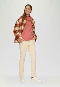 Rot und creme kariertes Jackett, rosa gestrickter Pullover, cremefarbene Hose und weiße Sneakers. Das Outfit bietet eine entspannte Passform und weiche Texturen.