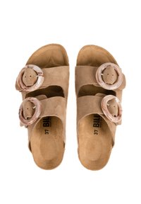 Sandales en daim marron avec deux larges sangles, chacune ornée d'une boucle circulaire à motifs. La semelle intérieure est douce et a une forme moulée pour plus de confort.