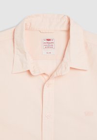 Camisa slim fit de color rosa claro con cuello estándar, botones en la parte delantera y pequeño logo bordado en el pecho. El material parece liso.