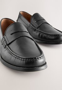 Mocassini neri in pelle con dettagli cuciti, texture liscia, punta arrotondata e suola in gomma a profilo basso. Design classico senza lacci.