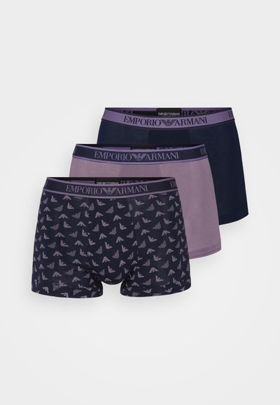 Três pares de boxers da Emporio Armani: um em azul marinho sólido, um em roxo claro sólido e um com padrão de pequenos triângulos sobre um fundo escuro.