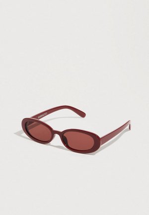 Lunettes de soleil ovales rouges avec des verres semi-transparents et une monture en plastique lisse. Les branches sont fines, ornées d'un logo blanc.