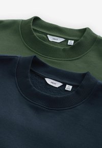 Twee crewneck sweatshirts, één donkergroen en één marineblauw, met ribgebreide kraag en labels die maat en merk aangeven.