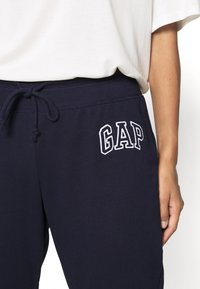 Mörkblå mjukisbyxor med dragsko i midjan, med broderad vit "GAP"-logotyp. Mjukt bomullsmaterial, avslappnad passform och sidofickor.