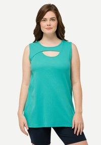 Una blusa sin mangas de color teal con un escote redondeado y detalles recortados. La tela es suave y elástica. Llevada con pantalones cortos oscuros, crea un look casual.