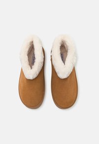 Pantofole in suede marrone con una morbida e soffice fodera bianca, forma arrotondata e design senza cuciture. Nessun hardware o decorazione visibile.