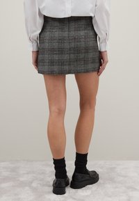 Karierte Minirock in Grautönen und Braun, mit tailliertem Schnitt und glatter Textur, kombiniert mit schwarzen Schuhen und Socken.