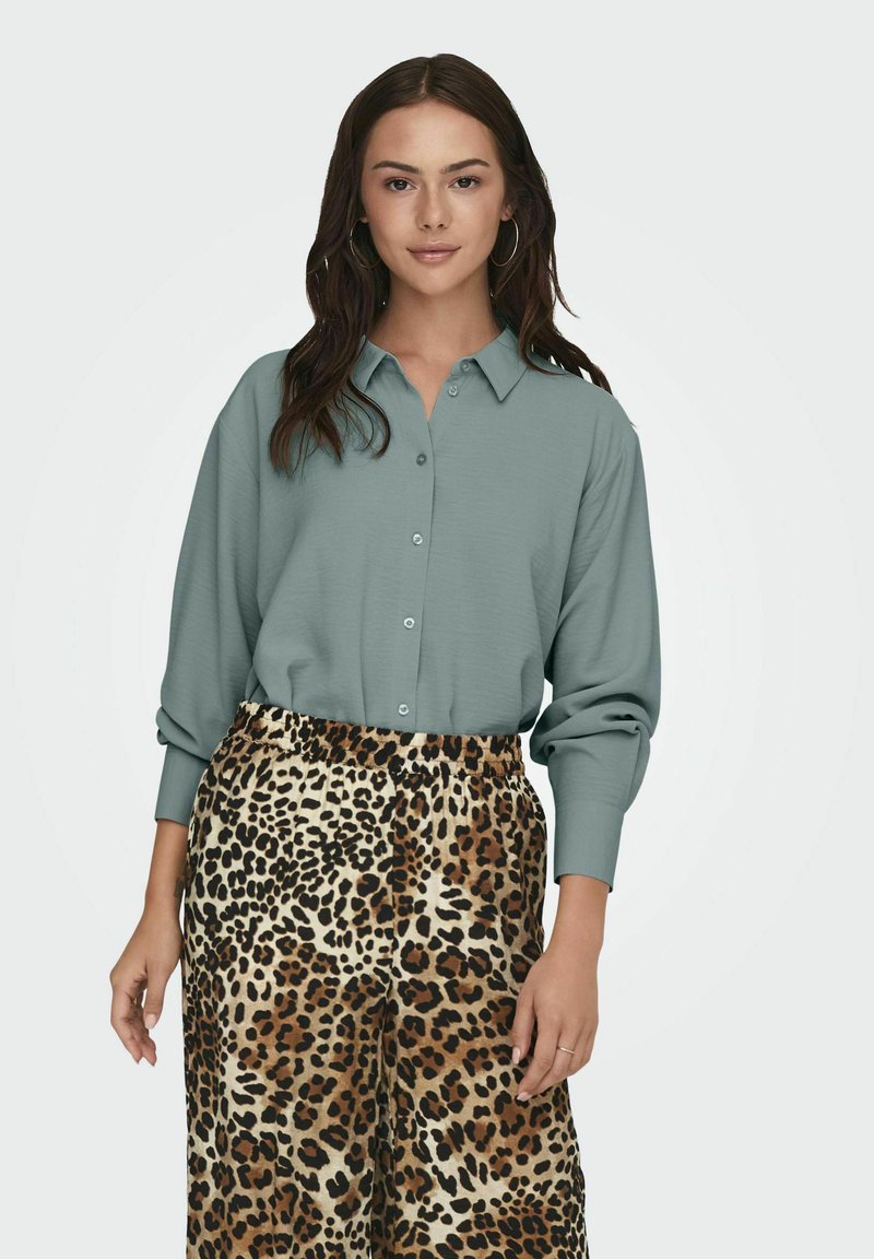 Light teal button-up shirt with loose sleeves paired with leopard print pants, featuring a relaxed fit and elastic waistband.