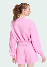 Ružová mikina s krátkym strihom, dlhými rukávmi a rebrovaným lemom, skombinovaná s ružovými šortkami v rovnakom odtieni. Hladká tkanina s voľným strihom.