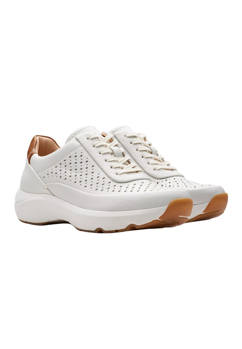 Zapatillas deportivas ligeras de color blanco con diseño perforado, punta redonda, detalles en beige y suela de goma marrón en contraste.
